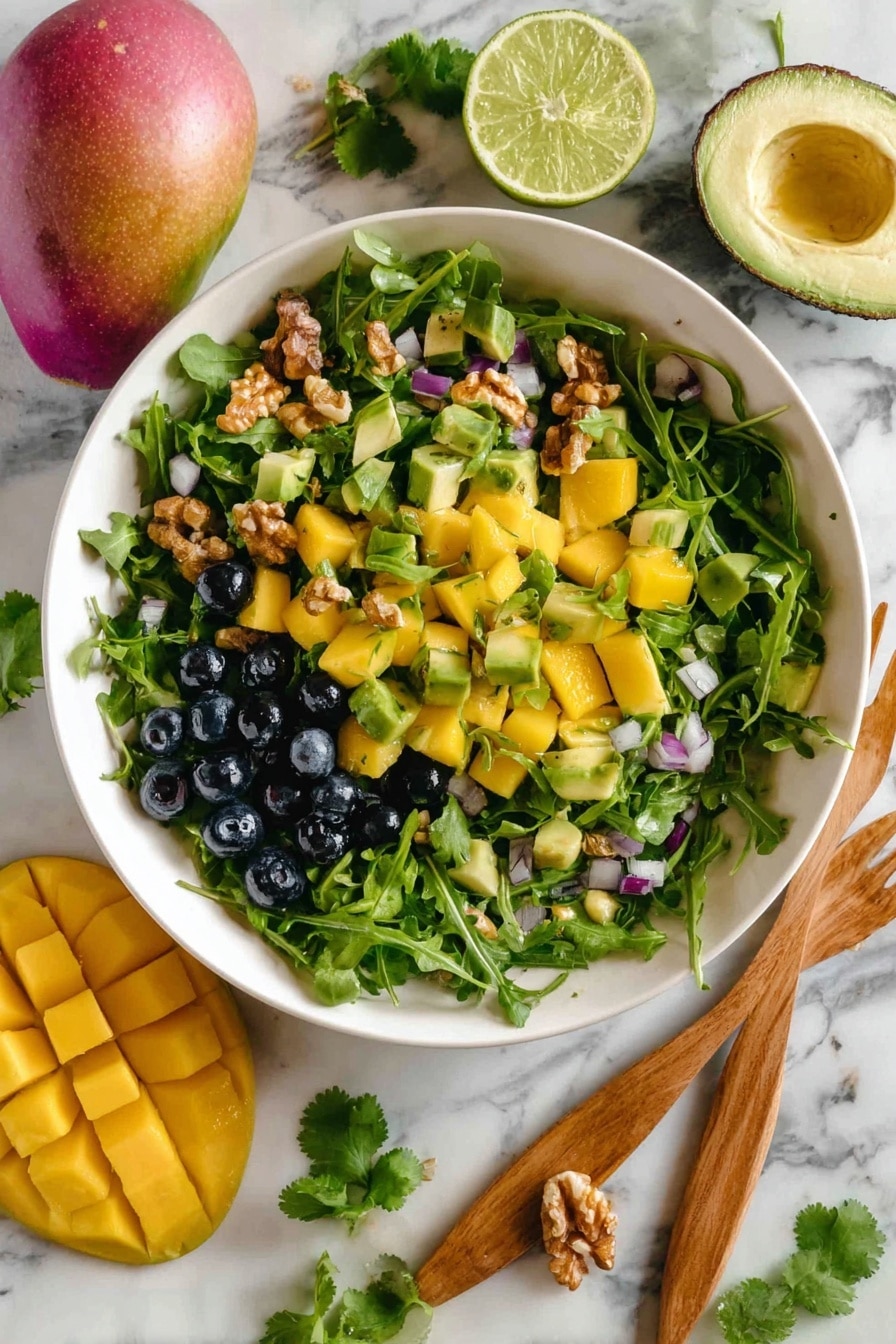 A white bowl filled with a vibrant salad sits on a white marbled surface. The salad has three main layers: a base of bright green leafy arugula, topped with chunks of yellow mango and small dark blue blueberries scattered throughout. There are also pieces of green cucumber and small bits of red onion mixed in. On top, there are light brown walnut pieces and sprigs of fresh green cilantro evenly placed. Around the bowl, there are whole mangoes, a halved lime, a whole lime, and half an avocado. Next to the bowl is a wooden spoon and fork. Photo taken with an iphone --ar 2:3 --v 7 - Mango Cucumber Salad with Blueberries and Avocado, healthy fruit and veggie salad, fresh summer salad recipe, easy fruit salad ideas, refreshing tropical salad