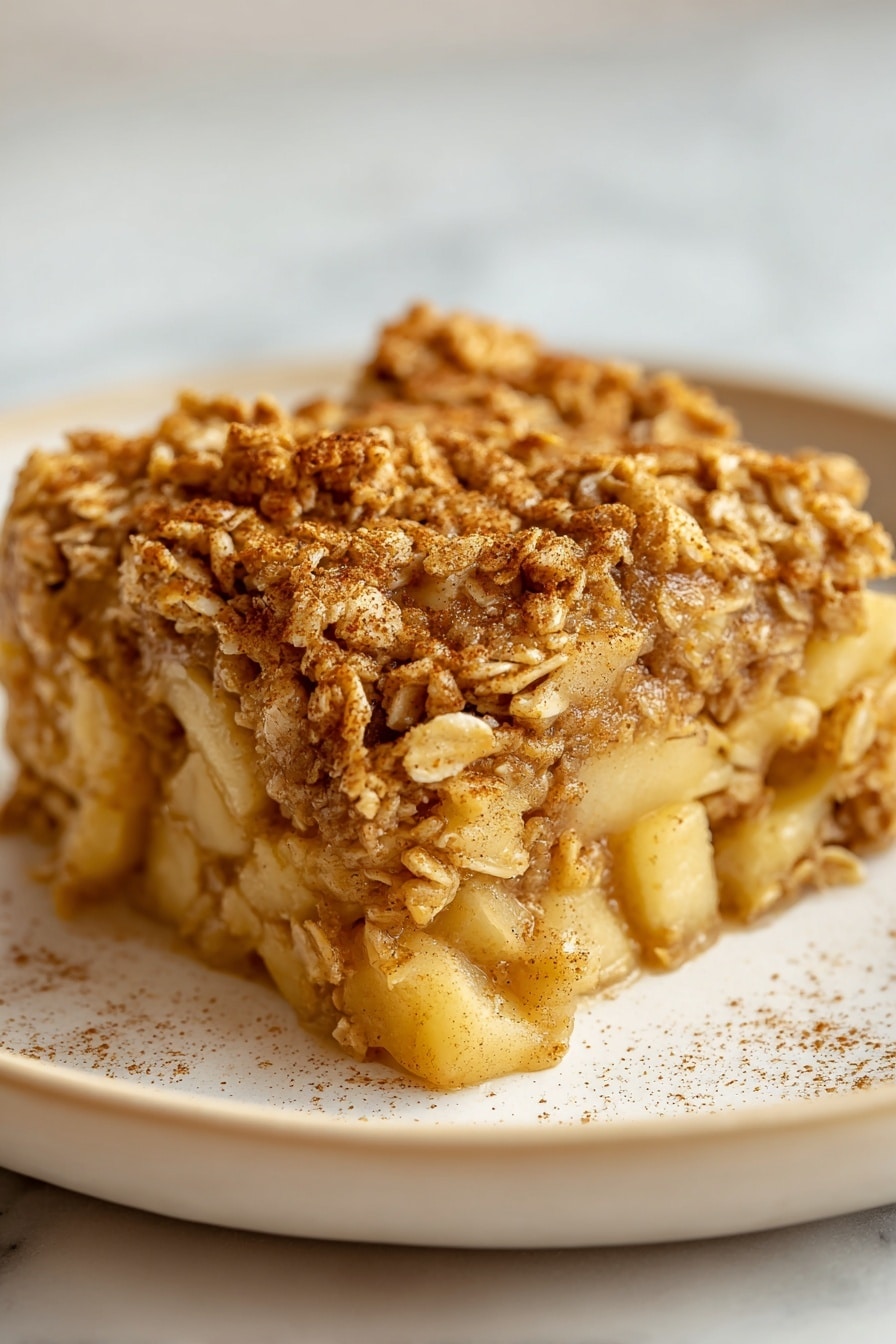 A close-up view of a single square oatmeal bar being held above a white baking dish filled with more oatmeal bars. The oatmeal bar has a golden-brown top with a slightly crispy texture and visible oats, while the inside looks soft and moist with a light tan color. The bars in the dish are cut into even squares, showing layers of oats throughout. The white baking dish sits on a white marbled surface, giving a clean and bright background. photo taken with an iphone --ar 2:3 --v 7 - Apple Cinnamon Baked Oatmeal, cozy breakfast recipes, healthy baked oats, easy breakfast ideas, cinnamon apple oatmeal
