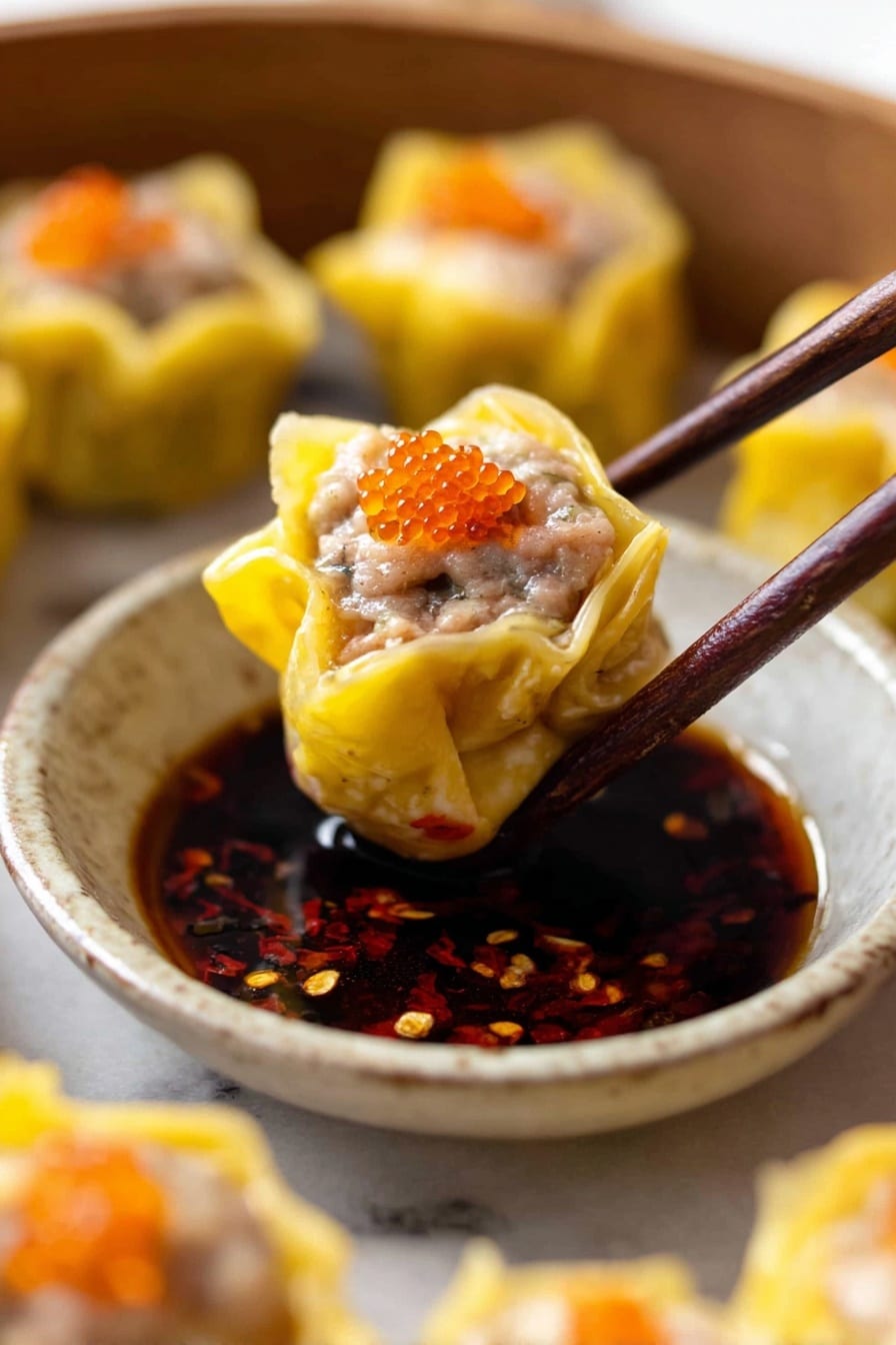 A close-up view shows a yellow dumpling held with dark brown chopsticks above a small round white ceramic bowl filled with dark soy-based dipping sauce speckled with red chili flakes. The dumpling has a soft yellow wrapper folded open at the top, revealing grayish ground meat inside, topped with small bright orange fish roe. Around the bowl are several more similar dumplings on a white marbled surface, slightly blurred, maintaining the focus on the dumpling being dipped. photo taken with an iphone --ar 2:3 --v 7 - Steamed Siu Mai Dumplings, Dumpling recipes, Asian dim sum, Pork shrimp dumplings, Steamed Chinese dumplings